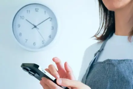 工事の予定時間を時計とスマートフォンで確認する女性